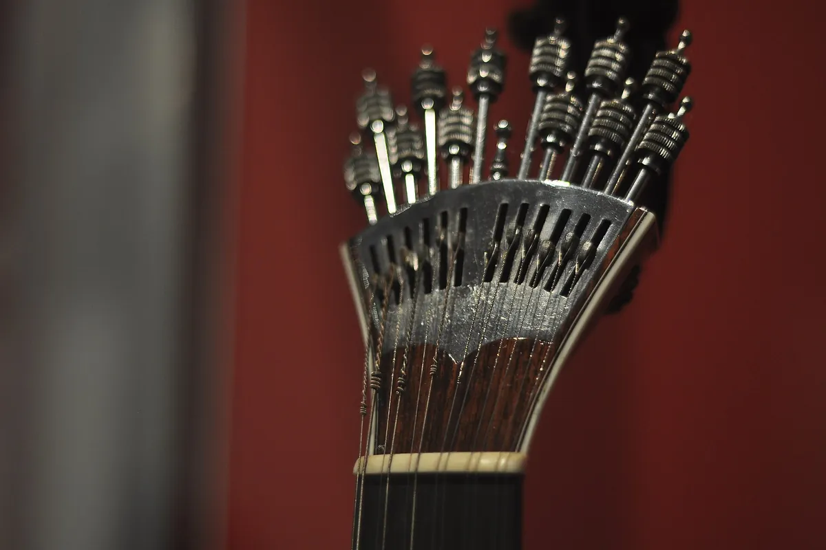 A close view of the silver watch-key tuning mechanism of a Portuguese guitar against a red background.