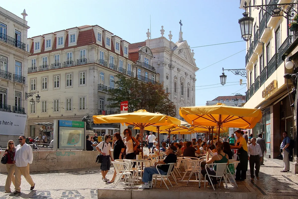 Yellow parasols over café tables on Largo do Chiado, with pale historic buildings behind.